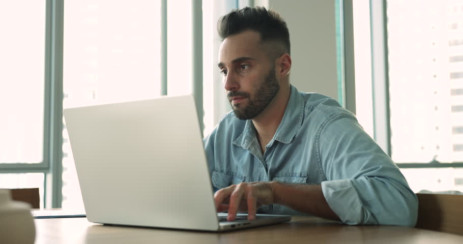 Handsome smiling Hispanic man sit at desk using laptop, web surfing information, spend time on internet, chat or work online looks satisfied with remote telework. Modern technology usage, e-commerce Royalty-Free Stock Footage #1109599913