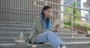 Young African American woman student or freelancer watching online lecture or conference using tablet pc pad computer sitting outdoor