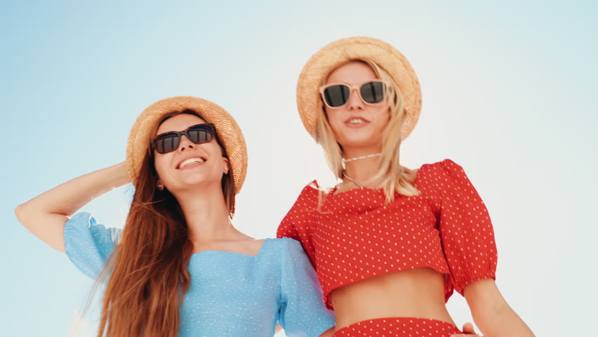 Two young beautiful smiling hipster women in trendy summer same clothes. Carefree models posing in the street. Positive models having fun. Cheerful and happy, at sunny day. In hat and sunglasses