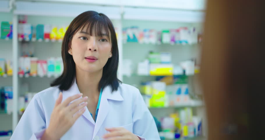 Young Asian pharmacist talking with customer at pharmacy counter. She tells customers about drug information at the pharmacy.