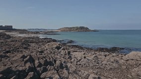 Grand Be islet seen from Saint-Malo rocky shore, Brittany in France. Aerial drone flying low altitude and sky for copy space