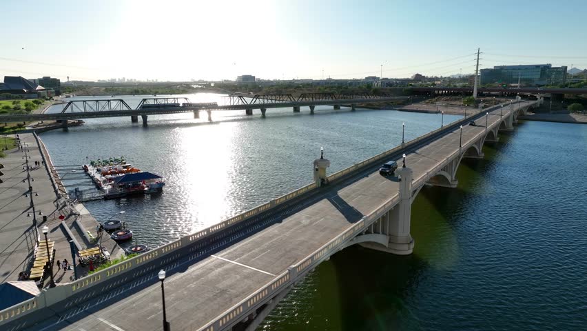 Tempe Bridge over Salt River and Tempe Town Lake in Tempe, Arizona. Aerial shot of bridge and traffic during bright sunset in AZ reflected by water. Royalty-Free Stock Footage #1109612245