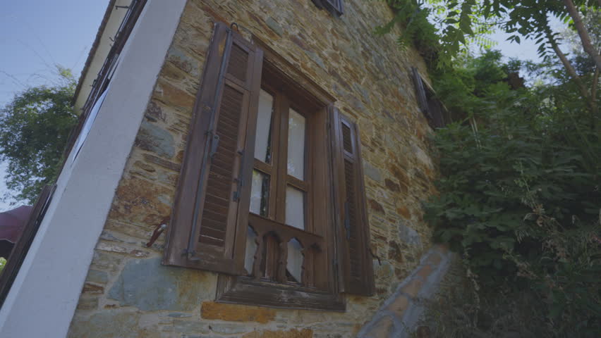Brown wooden window in two-storey stone house in tropical village. Windowsill with small fence covering lower part of window low angle shot