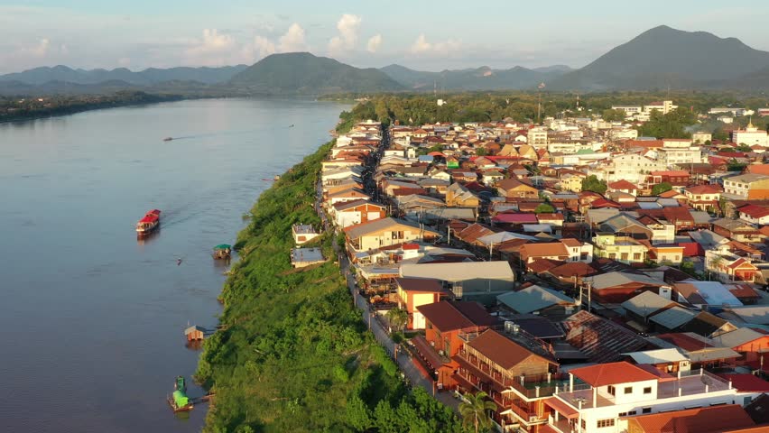 Chiang Khan, Thailand, the aerial view of the Mekong river and the riverside village that has a local road passed the residential zone, with the mountains and the blue sky in the background. Royalty-Free Stock Footage #1109616907