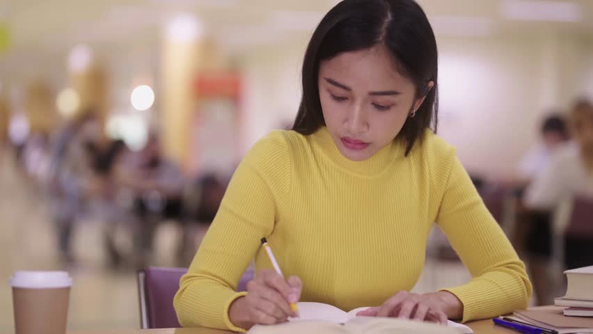 Cute smart Asian girl student writing notes preparing for college test in notebook, making summary for class report. Learning workplace for exam in library table