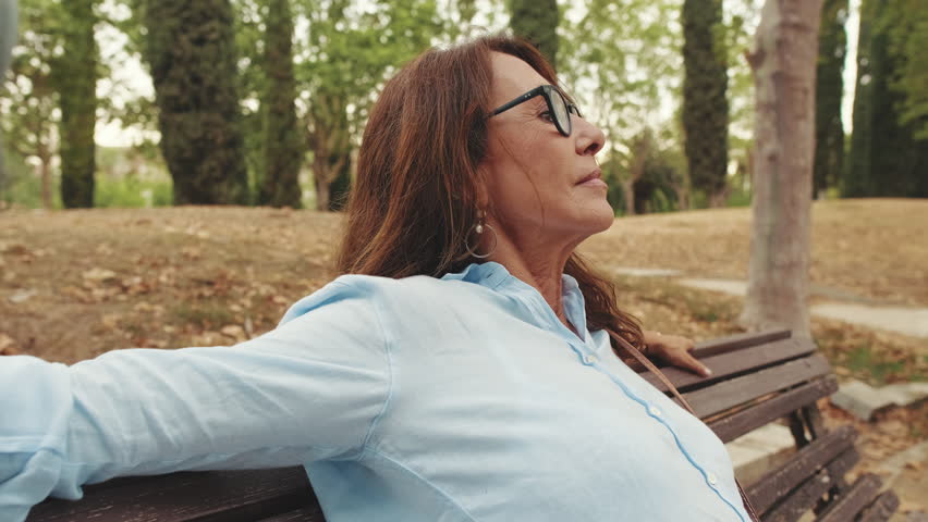 Close-up of beautiful retired woman with glasses having rest relaxing while sitting in the park