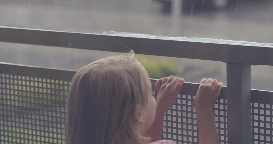 Funny kid girl 4-5 year old happy about the rain outside the window. Happy peaceful childhood. Summer.