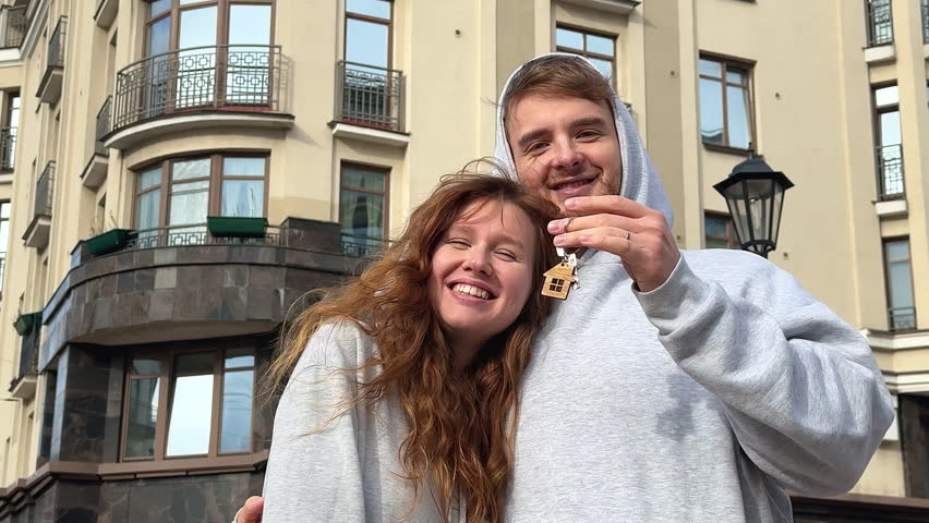young married couple with keys to a new apartment against the background of the house