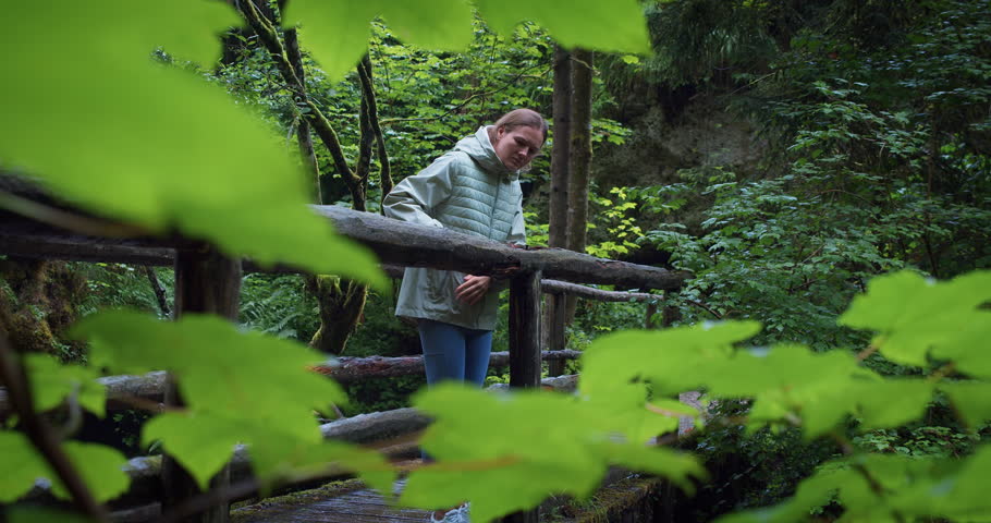 Woman watching nature during rain on a wooden bridge in the forest. Overcast spring or summer.