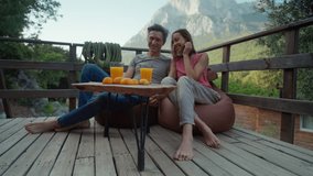 happy joyful couple at sunny morning outdoors in mountain camping enjoying sunrise and drinking fresh orange juice. traveling, wellbeing and healthy nutrition concept. bungalow with terrace in nature - Powered by Shutterstock - Get 15% off with code: PIKWIZARD15