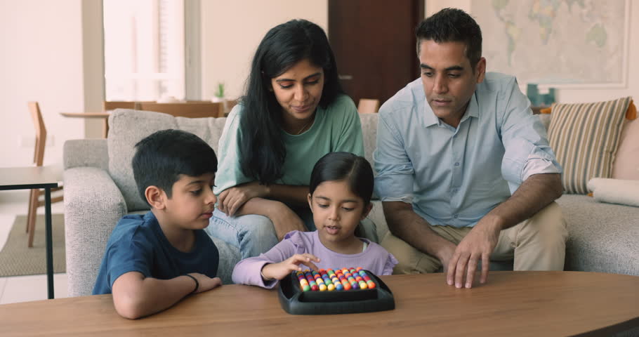 Young Indian parents and little children play modern rainbow balls boardgame in cozy living room at home, spend carefree leisure and communication together. Family fun, hobby, intellectual activity Royalty-Free Stock Footage #1109628315