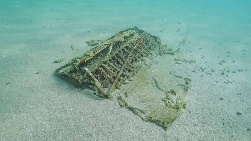 Camera moving forwards to discarded old sofa lying on sandy seabed in sun glare, Mediterranean sea, Slow motion. Concept pollution of the Ocean