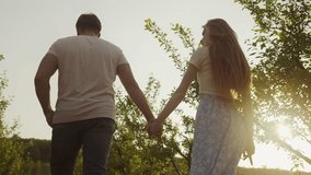 Back view of a couple in in love enjoying each other while walking in the orchard, holding hands. The man holds the woman's hand. Family relationships - Powered by Shutterstock - Get 15% off with code: PIKWIZARD15