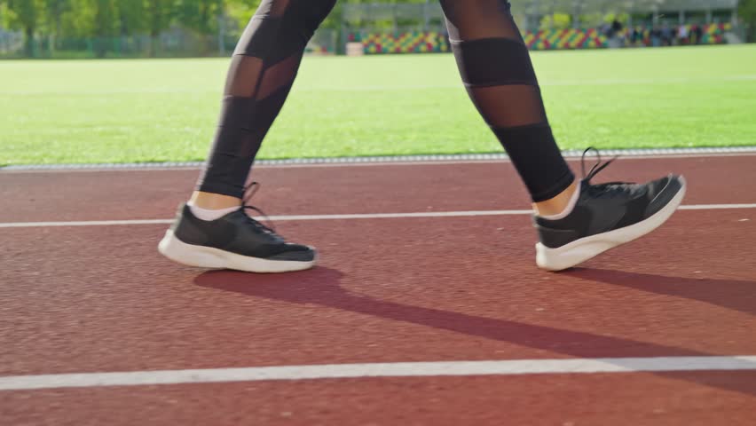 Side view legs of sportswoman walking on red sports track. Camera follows young sporty woman. Healthy lifestyle concept. Unrecognizable person. Close-up in 4K, UHD Royalty-Free Stock Footage #1109631347