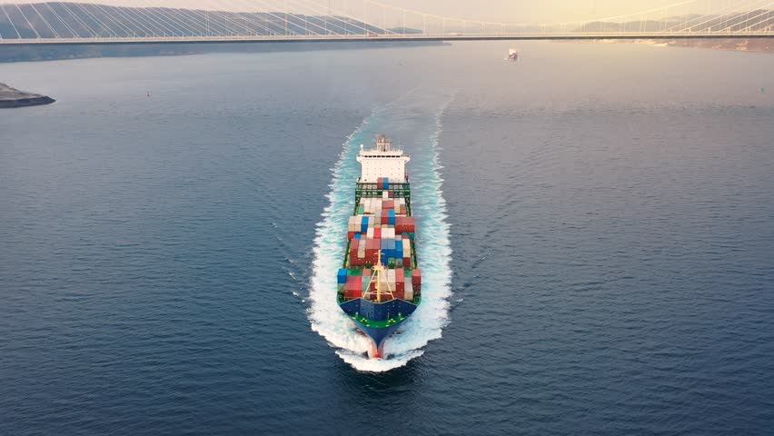 Front of container ship bow, cargo ship or nautical vessel underway at full speed through calm water. Bulbous bulb breaks waves. Forecastle, colorful boxes, upper deck, wheelhouse of ocean liner
