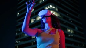 Low angle cinematic shot of attractive African American female puts on VR virtual reality metaverse headset at night city on blurred background. Multi racial young woman using AI goggles helmet online - Powered by Shutterstock - Get 15% off with code: PIKWIZARD15