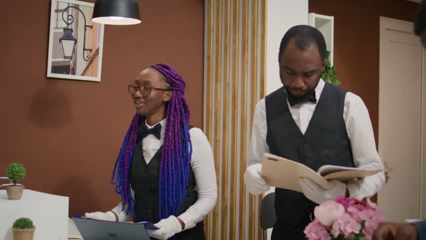 Couple registering with signed forms at reception, asking hotel front desk staff about facilities and ammenities. Concierge employee offering assistance for customers, tourism industry.