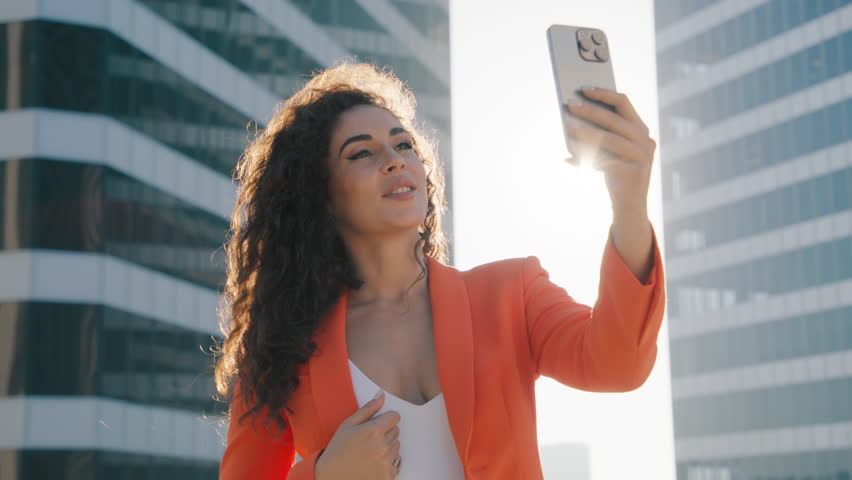 Happy african american woman influencer blogger using mobile cell phone, taking selfie, posting in social media apps, chatting with friends online on smartphone standing in downtown in golden sunshine Royalty-Free Stock Footage #1109636075