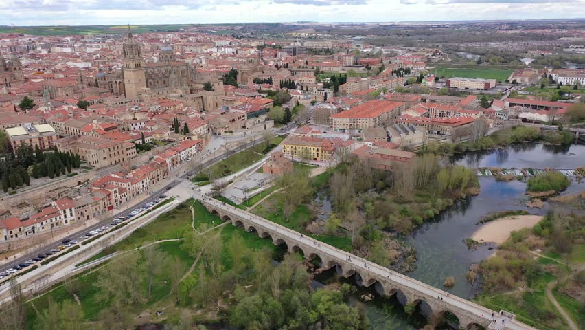 Scenic aerial view of Salamanca historic district overlooking gothic building of cathedral towering over residential buildings and ancient arched roman bridge across Tormes river in spring, Spain