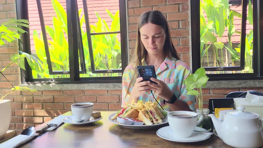 A young woman photographs her breakfast in a cafe in Bali, a young woman in a cafe photographs her breakfast on social media