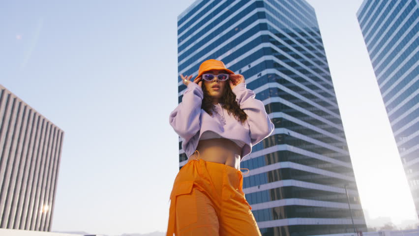 Low angle model enjoying modern dance. Trendy lifestyle, cool expression close up. Cinematic shot dancing woman young talented street style dancer performing freestyle hip hop moves in city