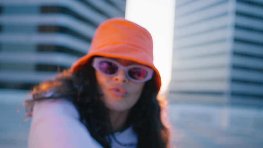 Funny stylish hipster girl. Fashion woman in trendy sunglasses and orange bucket hat dancing outside looking at camera. Outdoor portrait female dancer performing dance with freestyle moves Royalty-Free Stock Footage #1109637403