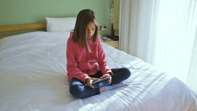 Girl playing video game on smartphone sitting on a bed in the morning. 4k slow motion video footage
