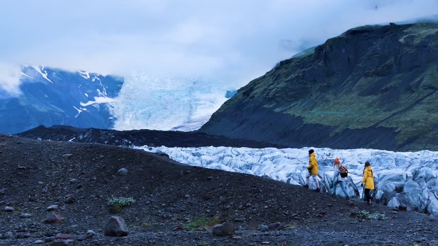 Three friends ( 2 women and 1 men) hiking and admire the marvelous glacier (Iceland). Aerial drone view.