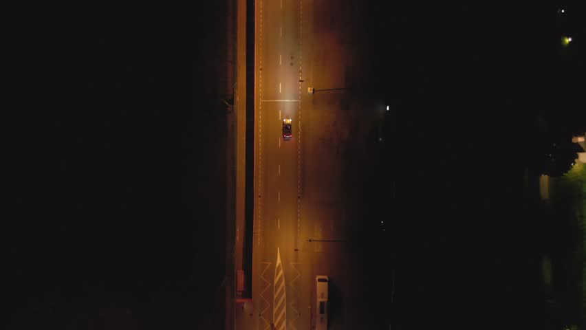 Aerial top down view following a car in a street during the night in Lugano, Switzerland. Cinematic drone shot over night city. Car headlights light up the road. Royalty-Free Stock Footage #1109641963