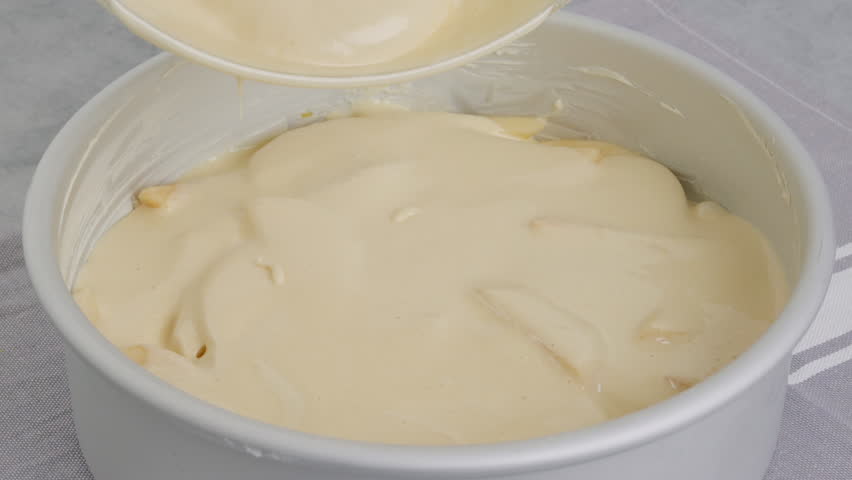 Chef pouring cake batter into a baking pan on the top of apple slices. Apple cake preparation process, recipe