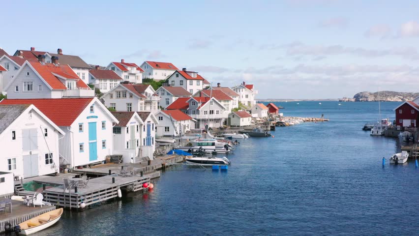 Fishing Village in Sweden flying past ocean front luxurious expensive real estate on Island. Private pier and jetty in open ocean channel or bay. Swedish Gullholmen exclusive houses