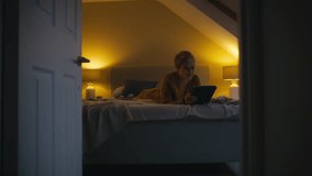 Laughing young woman lying on bed at home watching film, movie or social media post on digital tablet - shot in slow motion - Powered by Shutterstock - Get 15% off with code: PIKWIZARD15