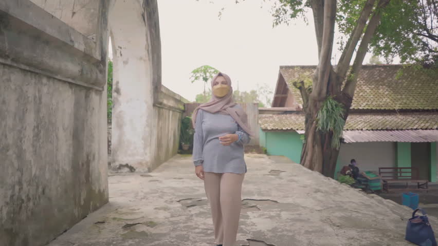 Front view of female with mask walking and entering new area framed by concrete gate