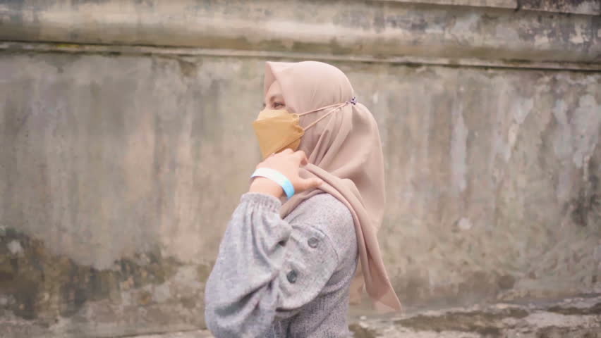 Side view of female with mask walking and enjoying view with concrete wall background
