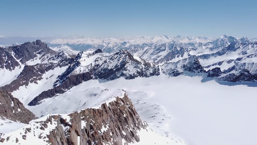 Beautiful cinematic aerial of snowy alpine mountain glacier peaks. Valleys and steep snow covered mountain ranges in distance. Drone flying forward, sunny day amazing landscape scenery view 4K