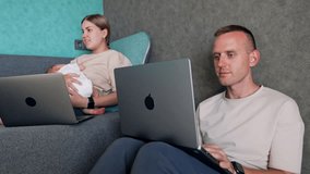 Busy modern parents of newborn working at home. Caucasian couple nurse their baby and work via internet.