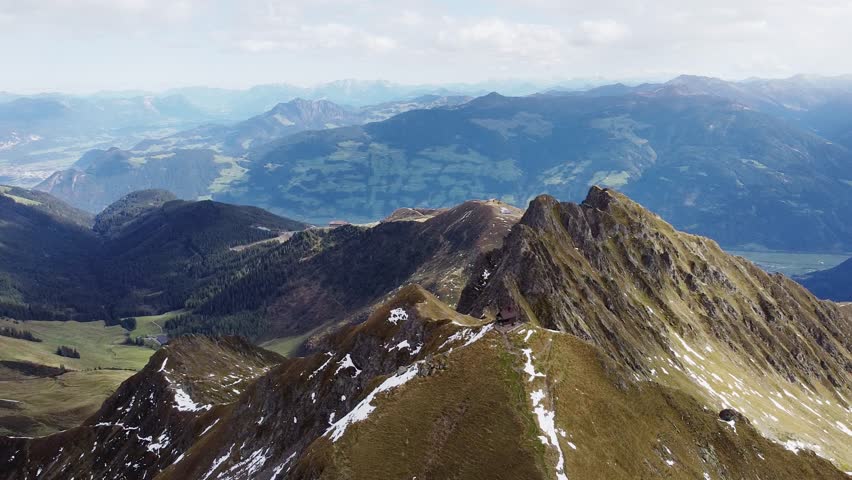 Cinematic aerial of alps mountain top with old wooden chapel on steep peak. Beautiful alpine scenery with valley in distance landscape view. Kellerjoch, Austria. Drone flying around summit, sunny day