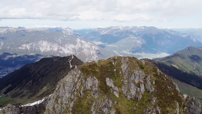 Cinematic aerial of alps mountain top with old wooden chapel on steep peak. Beautiful alpine scenery with valley in distance landscape view. Kellerjoch, Austria. Drone flying around summit, orbit shot