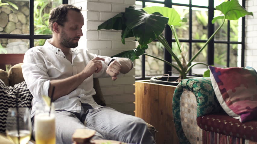 Young man with smartwatch drinking cocktail sitting in cafe
