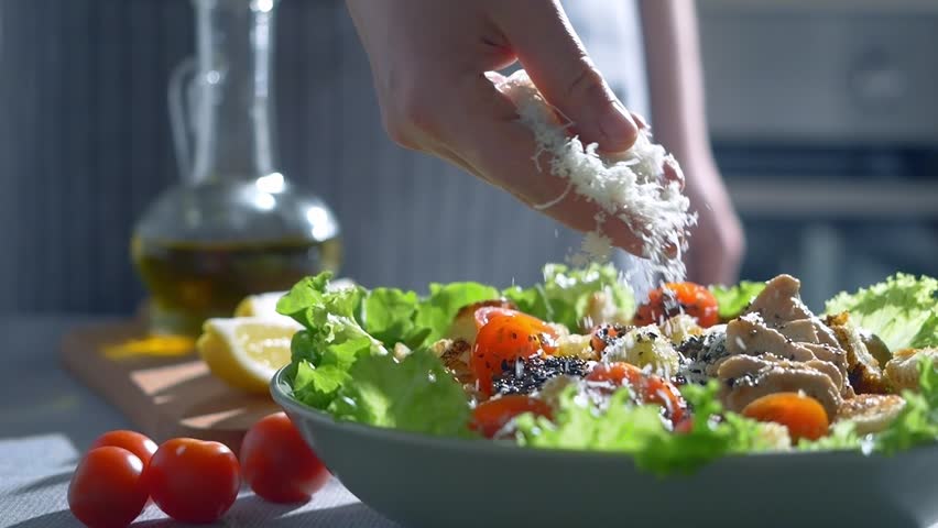 close up video of grated Parmesan cheese  falling on fresh green salad with lettuce leaves and tomatoes, slow motion. healthy salad bowl, homemade food. cheese traditionally made from cow's milk