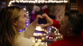 Back view of happy couple looking at fireplace through joined fingers making heart shape. Romantic Christmas eve celebration. Loving married spouses relationships, sincere feelings and love concept 4K - Powered by Shutterstock - Get 15% off with code: PIKWIZARD15