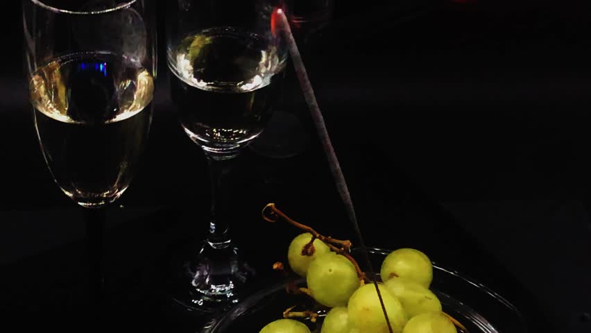 Glasses with sparkling wine swirling with white grapes surrounding firework sparkler light on christmas and new year look down camera movement