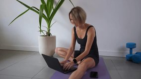Smiling woman using laptop for learning yoga through online tutorial while sitting in studio