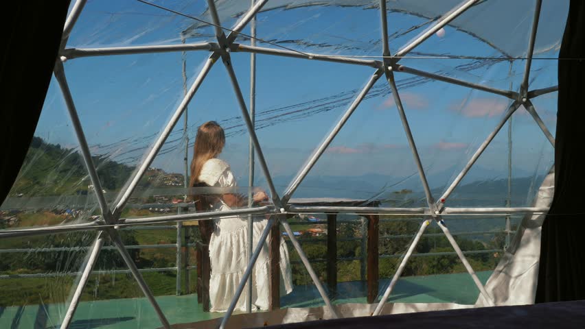 Woman relaxes in bubble tent, enjoying the peaceful mountain setting. Relaxing in a luxurious tent, with breathtaking mountain scenery as backdrop.