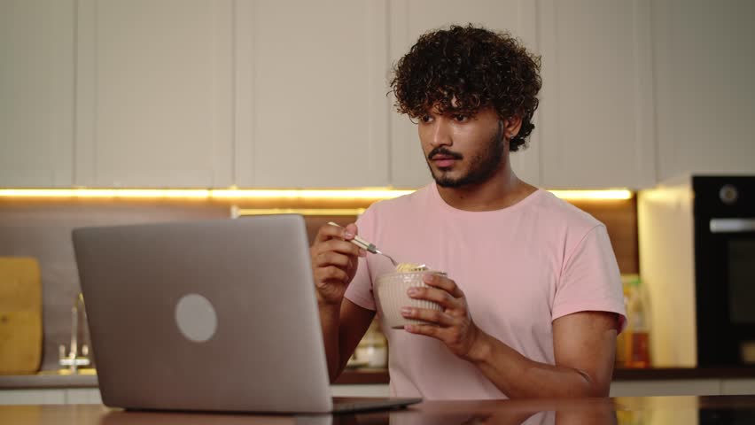 Young man working overtime eating ramen soup at home. Funny guy holding bowl instant noodles and watching video on computer. Male enjoying his food relaxed seeing series. Late night dinner Royalty-Free Stock Footage #1109674517