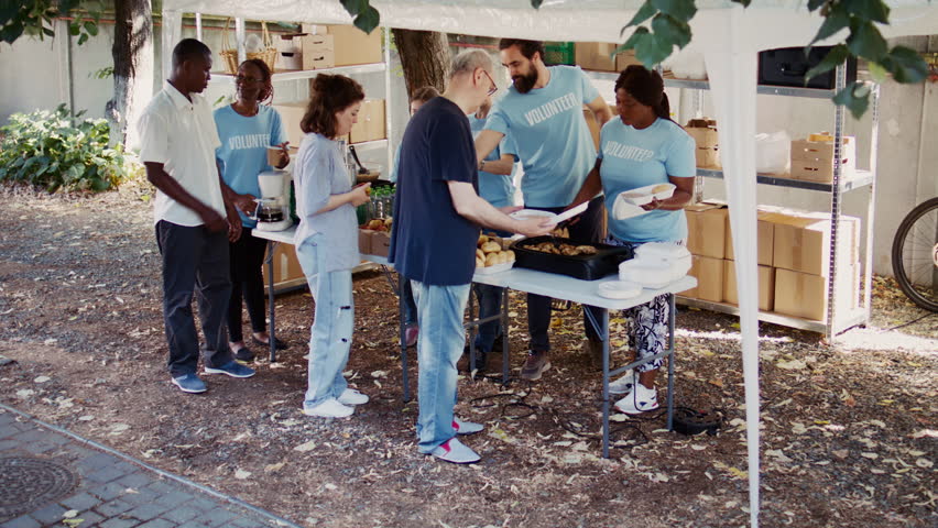 Multiracial volunteers engage in acts of charity by providing warm meals to underprivileged and homeless people. Non-profit group promote supportive atmosphere by extending essential aid to the poor. Royalty-Free Stock Footage #1109680787