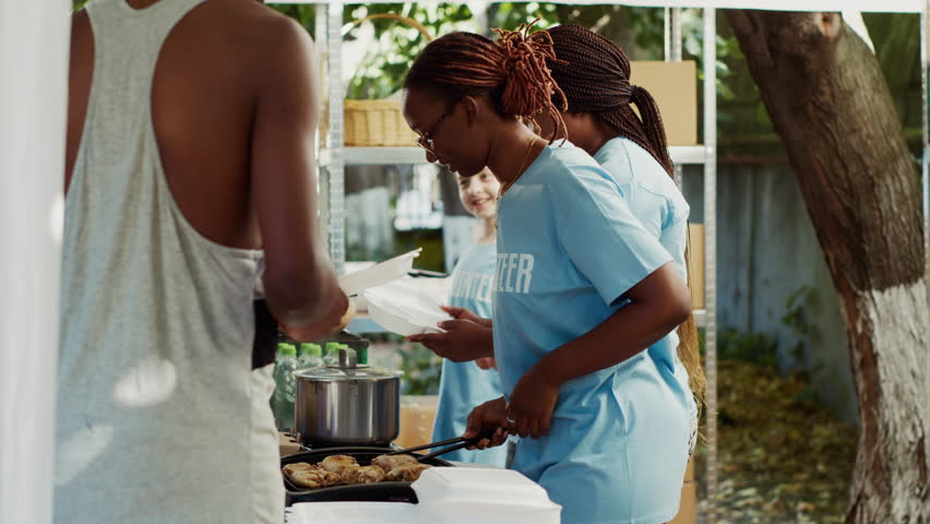 Young African American and Caucasian volunteers handing out free food and necessities to the less poor. At a homeless shelter, friendly charity workers give hunger relief and humanitarian help. Royalty-Free Stock Footage #1109680807