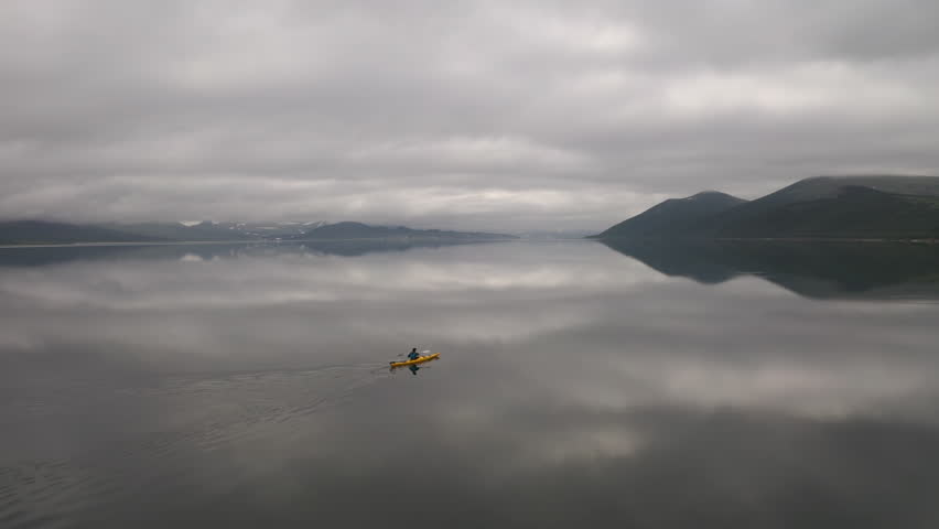 Aerial drone shot of a lone kayaker floats on the mirror-like surface of Lake Tolmacheva