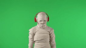 Green screen isolated chroma key video capturing a mummy wearing red headphones and dancing to the music with a smartphone in its hand.