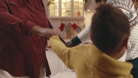 Cropped shot of happy African American family of three having fun together holding hands and round dancing near Christmas tree in their warm cozy apartmentの動画素材